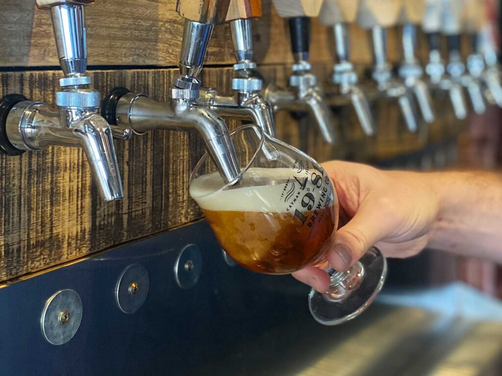 Hand pulling a pint of 19-81 Cayman beer from a tap at a brewery